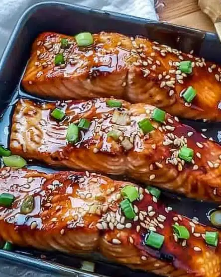 Baked teriyaki salmon garnished with green onions on a white plate.