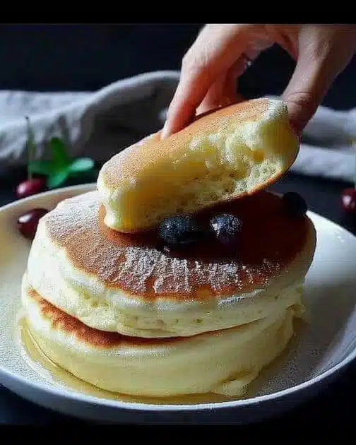 Fluffy Japanese soufflé pancakes stacked on a plate with syrup and berries.