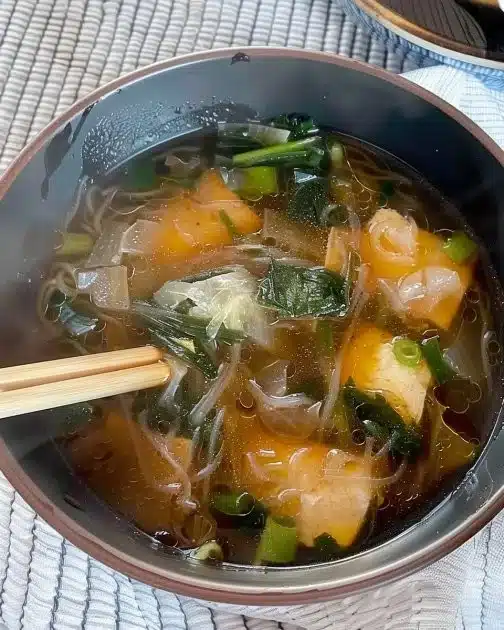 Bowl of delicious Japanese glass noodle soup with fresh vegetables and herbs.