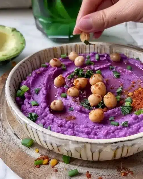 Bowl of purple sweet potato hummus topped with olive oil and herbs