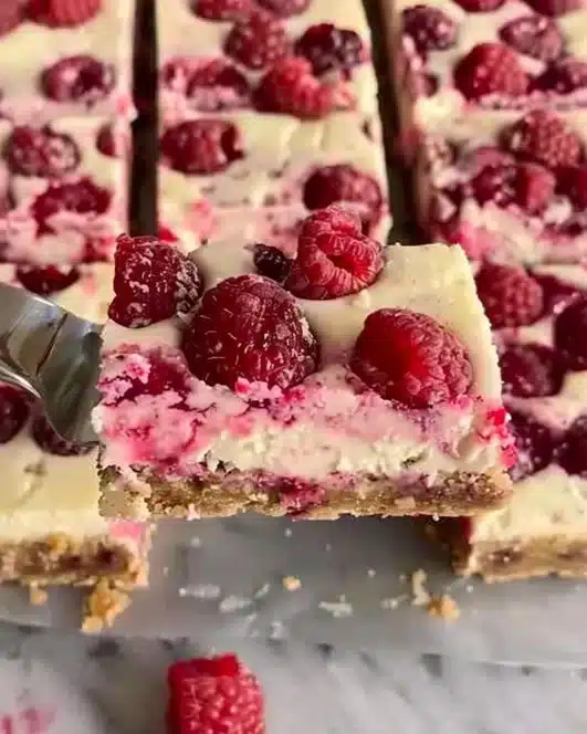 Delicious raspberry cheesecake bars with a creamy filling and berry topping